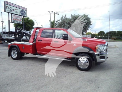 Ram 5500 tow truck with red cab and black tow equipment in yard, side view showing extended cab and steel wheels.