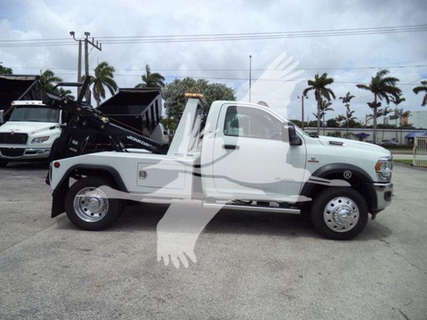 Truck side view of a white 2024 Ram SLT tow/winch truck with a black rear equipment bed and crane attachment; no visible textual labels readable.