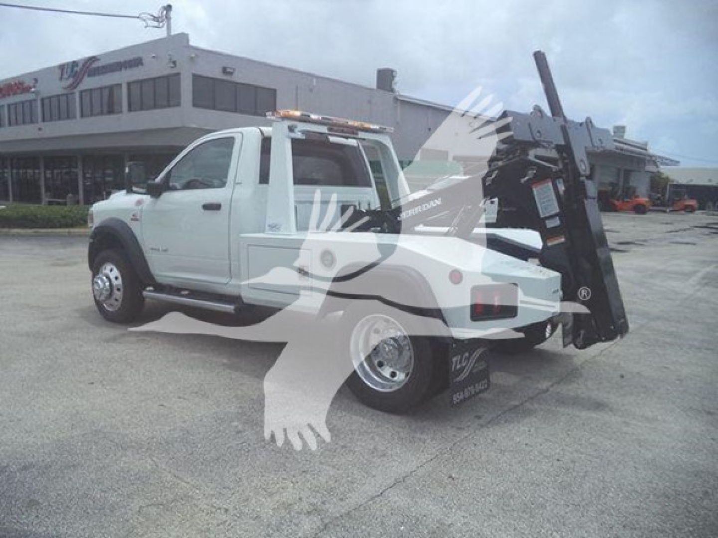 Ram pickup truck in service body with hydraulic winch and forklift-style lift on back, showing white cab and chassis and black metal equipment at rear.