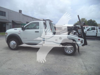 Ram tow pickup truck showing a winch system mounted at the rear with white cab, black winch arm, and dual rear tires; visible text includes 'RAM' on the side and a winch assembly at the back.