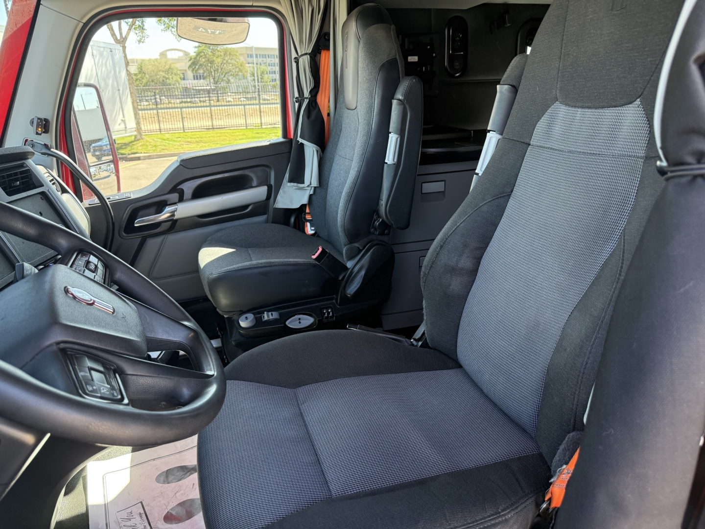 Truck cab interior showing driver's seat and passenger seat in a Kenworth T680, steering wheel, dashboard, and door panels visible.