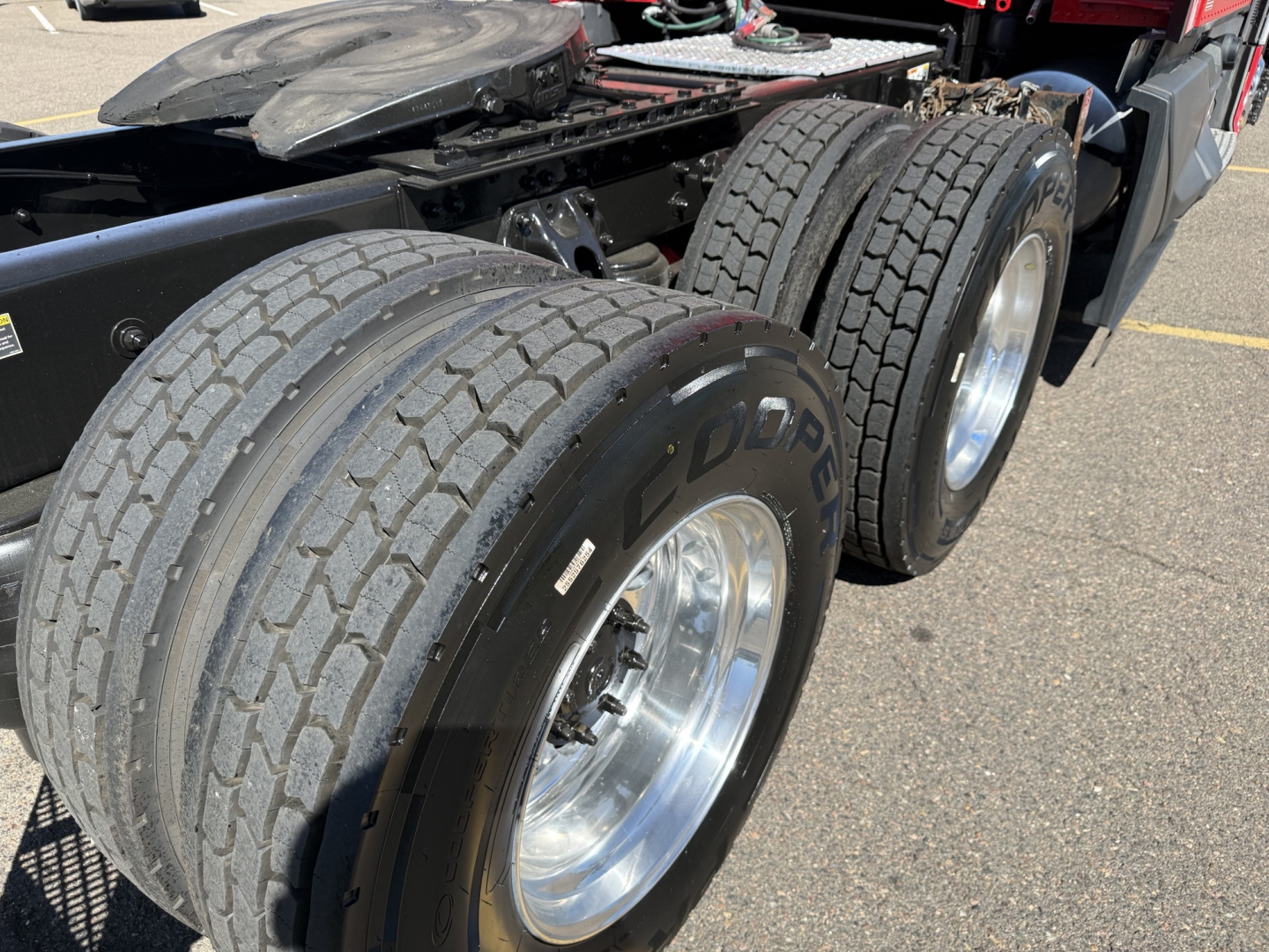 Kenworth T680 truck rear dual axle with large tires and chrome wheels, chassis frame visible, fuel/air lines and components near the fifth wheel mount.