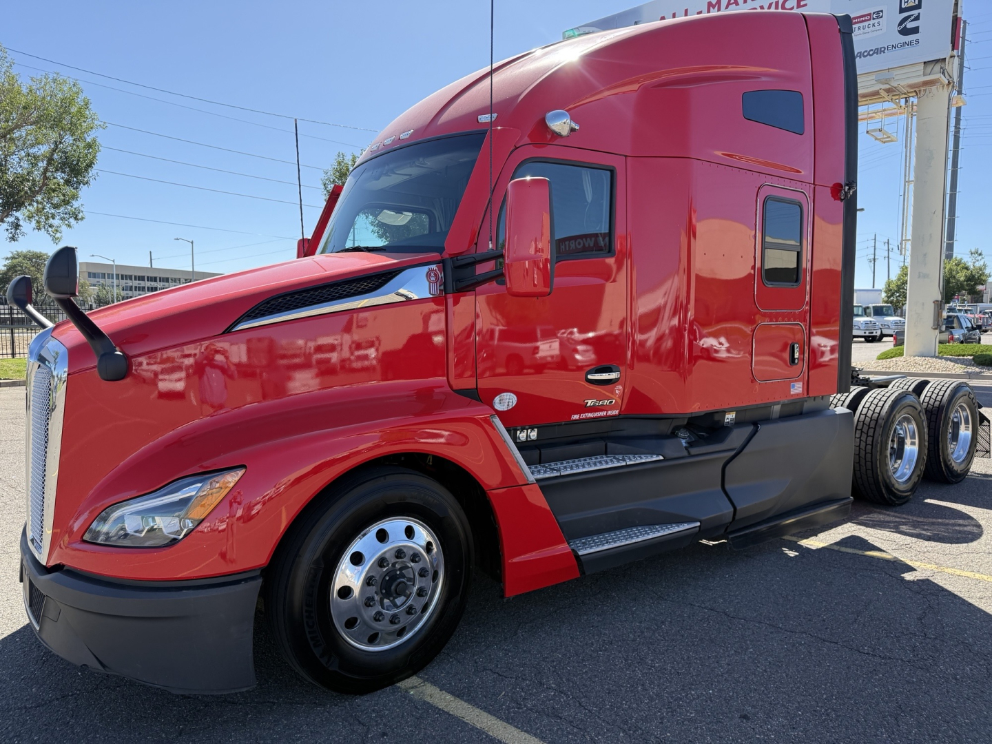 Kenworth T680 tractor in red, side view showing cab and front wheel with exhaust stack, no text reads clearly on components.