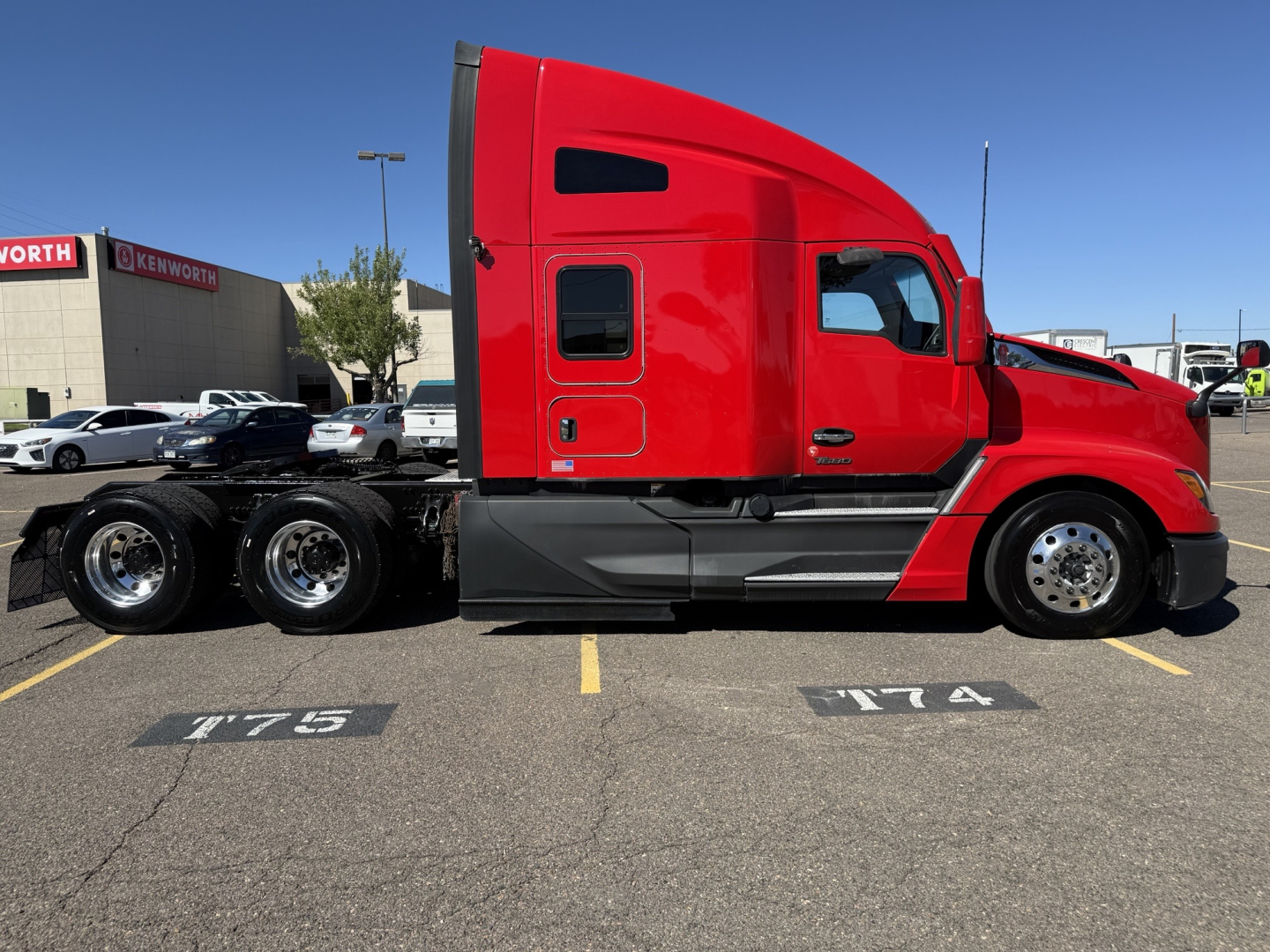Kenworth T680 sleeper cab in red side view showing tractor with dual rear axles, chrome fuel tanks, and black chassis in a parking lot.
