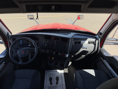 Kenworth truck cabin interior with steering wheel on left, dashboard gauges, center console, and red exterior visible through windshield.
