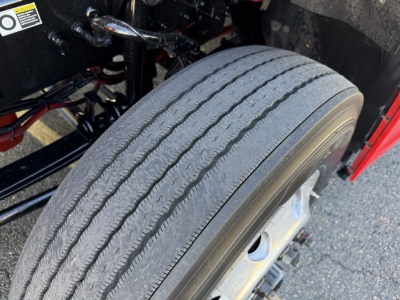 Kenworth T680 front wheel and suspension area showing large radial tire, part of truck chassis, with visible bolts and components.