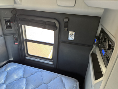 Kenworth T680 sleeper cab interior showing window with shade, door panel, seat/bed, control panel, and dashboard area.