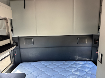 Kenworth T680 sleeper cab rear interior showing fabric headliner, storage compartments, and a blue quilted mattress in the sleeper area.