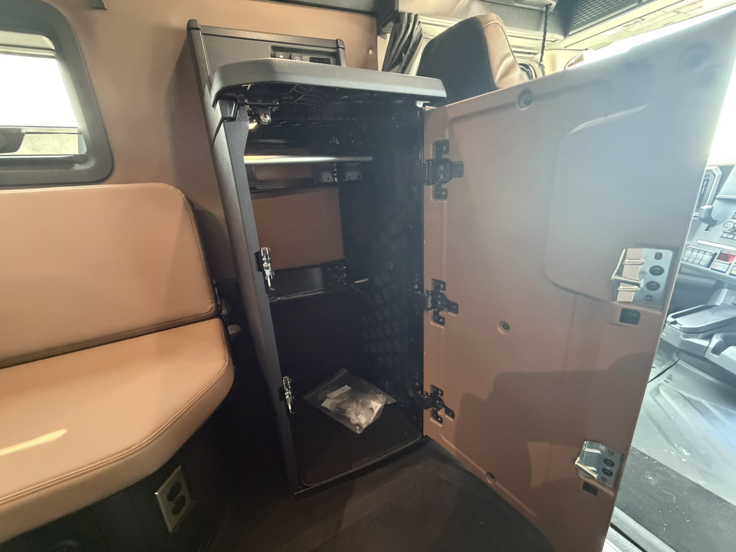 Cab interior showing a small cabinet or refrigerator unit inside a Mack PR64T76H sleeper cab door open, shelves and a few items visible.