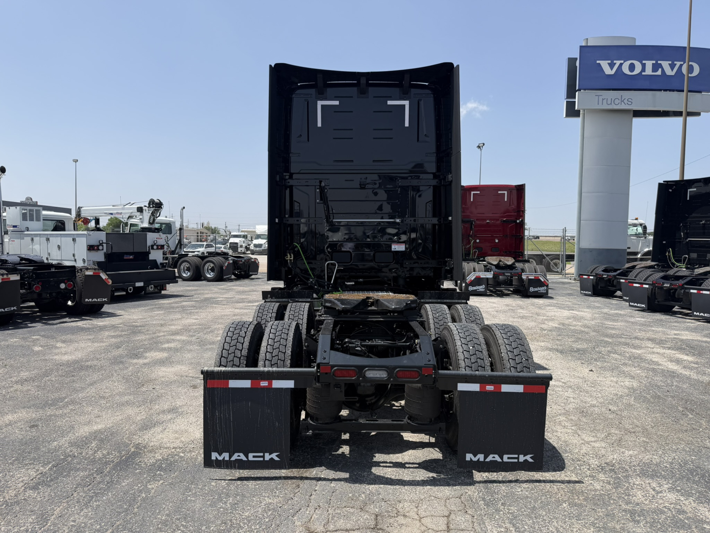 Rear view of a new Mack PR64T76H semi truck in a dealership lot showing dual rear axles, mudflaps with Mack logo, and a high cab