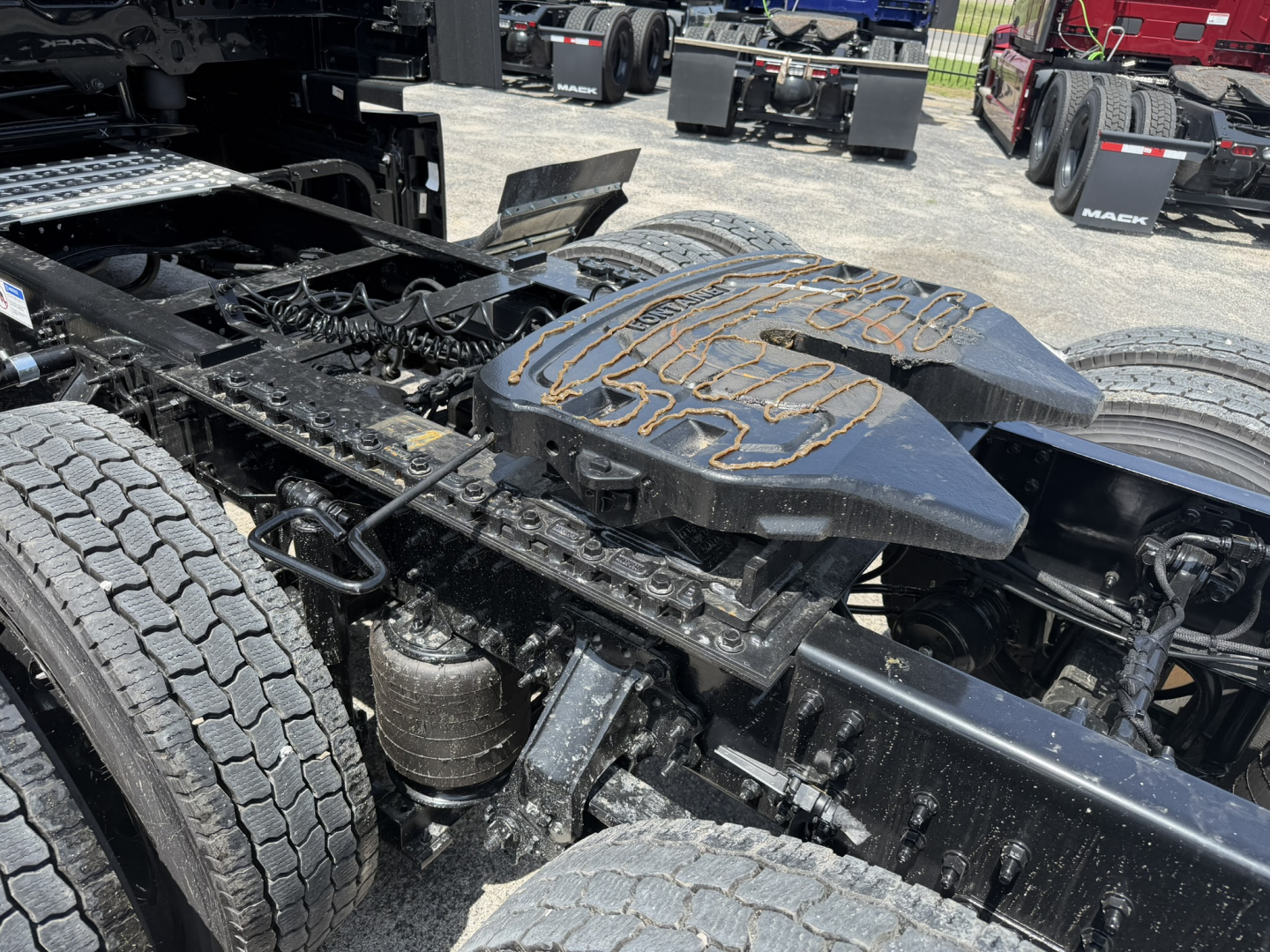 Truck chassis showing fifth wheel and dual rear tires with chassis rails and hydraulic components.