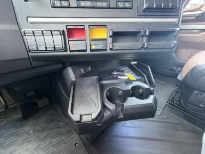 Dashboard and center console of a Mack truck showing switch controls, cup holders, and storage with key in ignition.