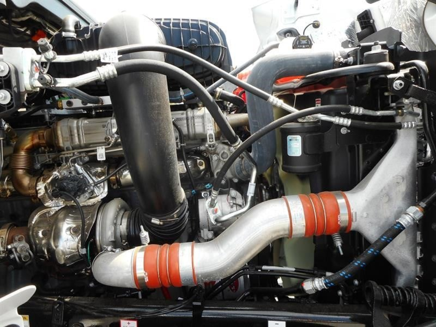 Western Star 49X engine bay showing intake piping and hoses with metal exhaust/air components and coolant reservoir.