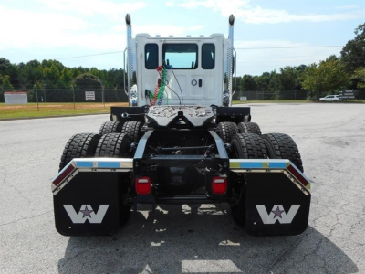 Rear view of a 2027 Western Star 49X day cab truck showing dual rear axles, mud flaps with Western Star logo, and chassis with reflective strips.