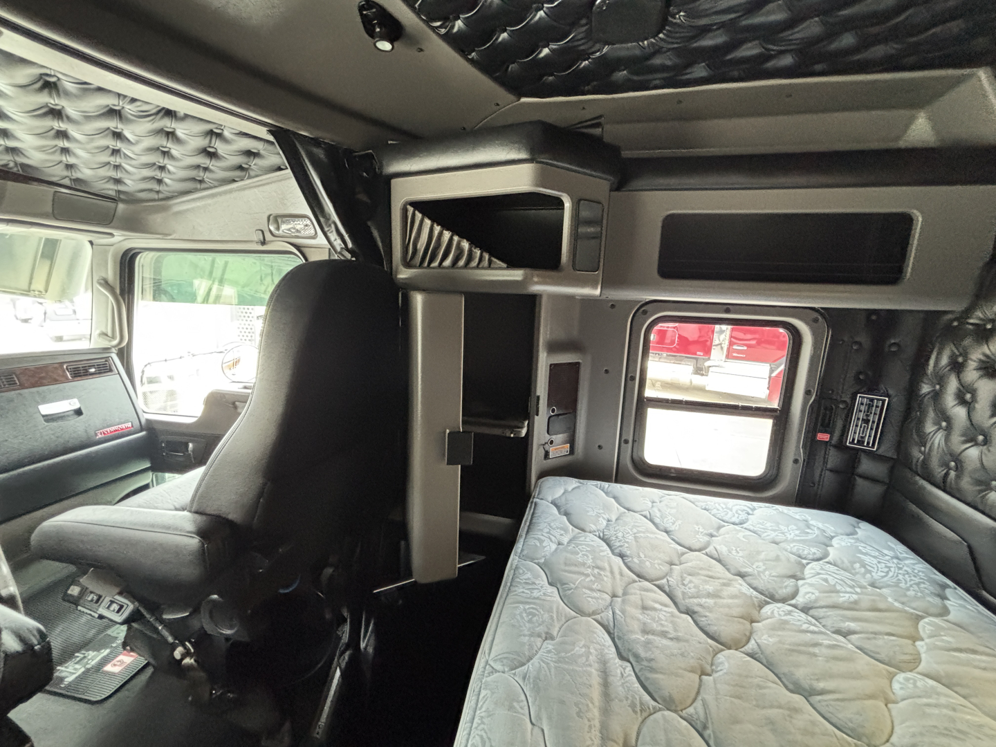 Kenworth W900L cab interior showing bunk area and control panel with quilted cab insulation and compact storage shelf.
