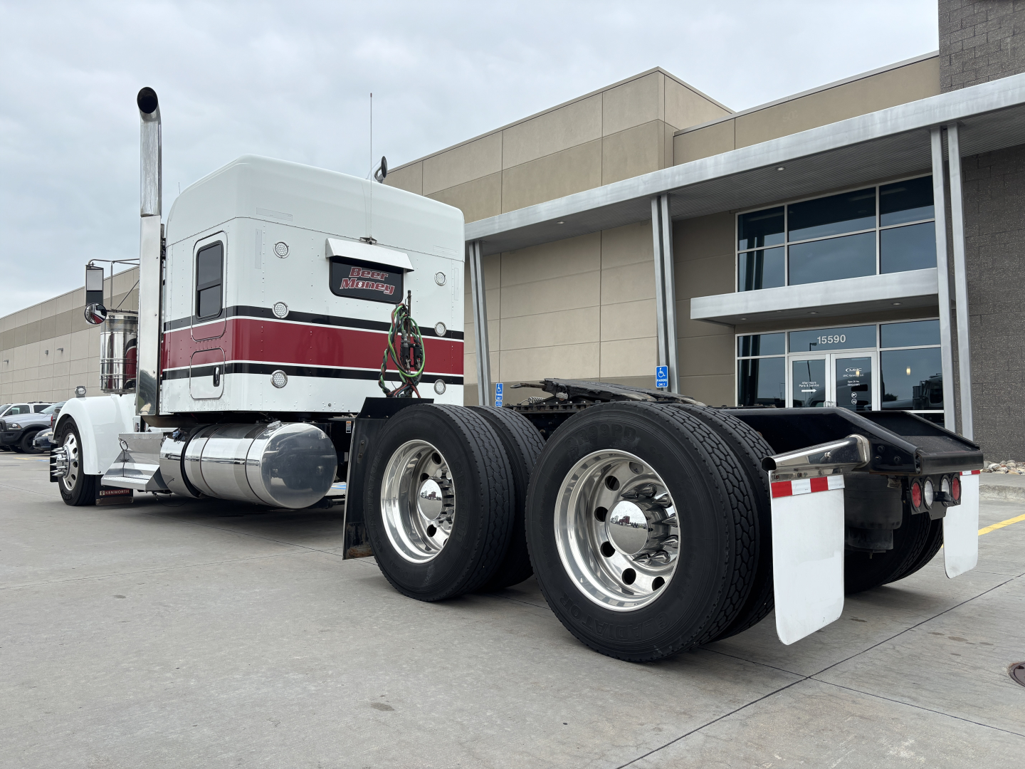 Kenworth W900L tractor rear/side view showing dual rear axles, chrome wheels, and sleeper cab with white and red livery.