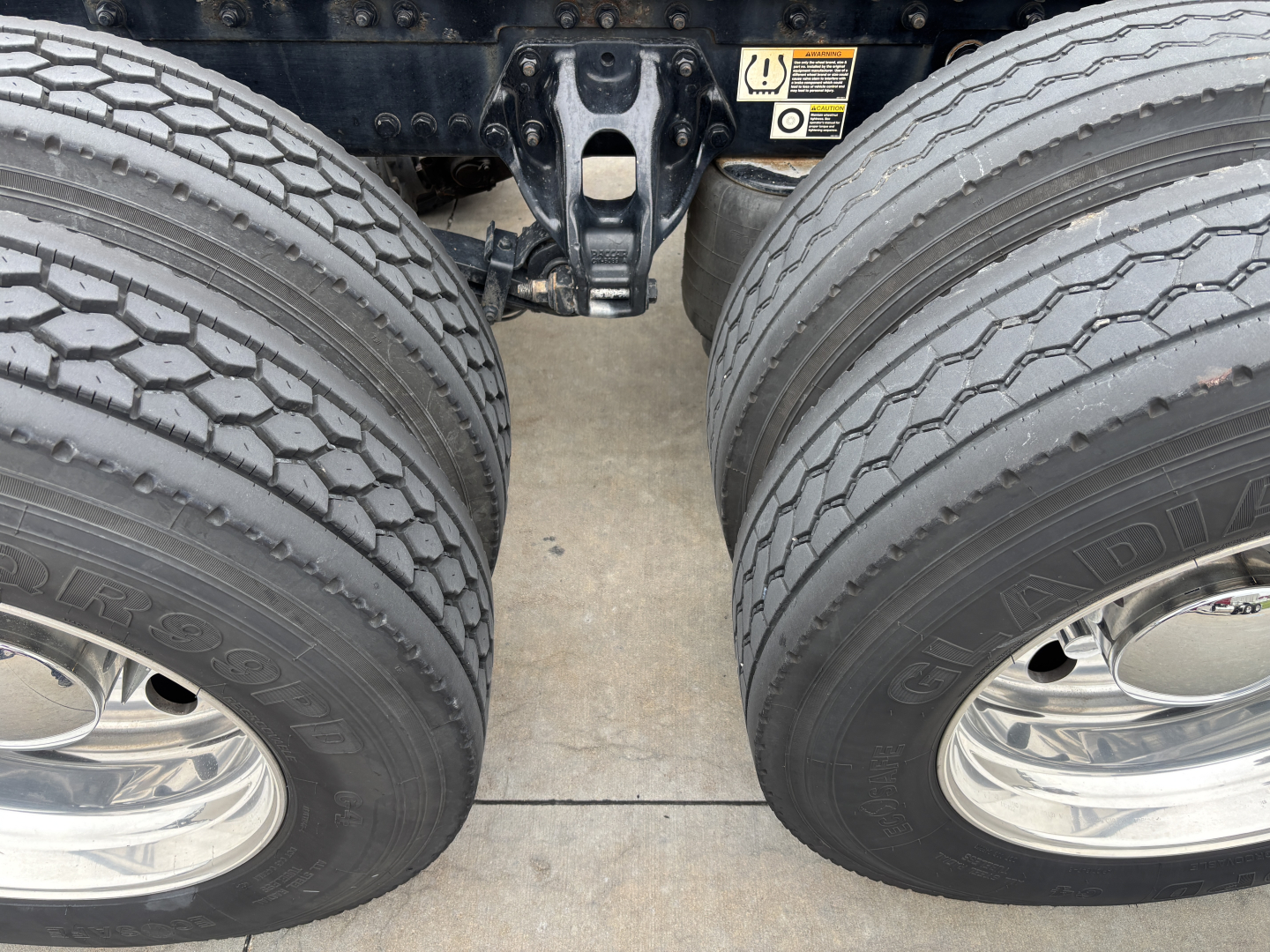 Dual rear tires of a Kenworth W900L tractor showing tread, chrome wheels, and a portion of the axle assembly between the two wheels.