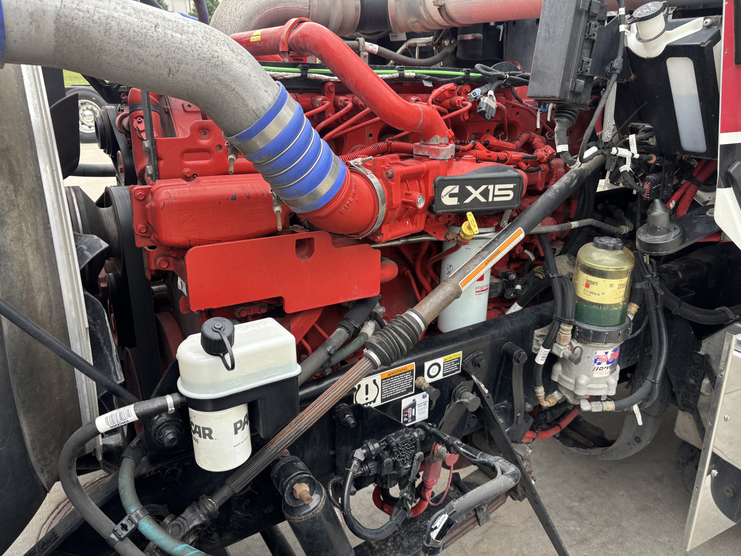 Kenworth W900L engine bay showing Cummins ISX15 engine with red block, coolant reservoir, and hoses.