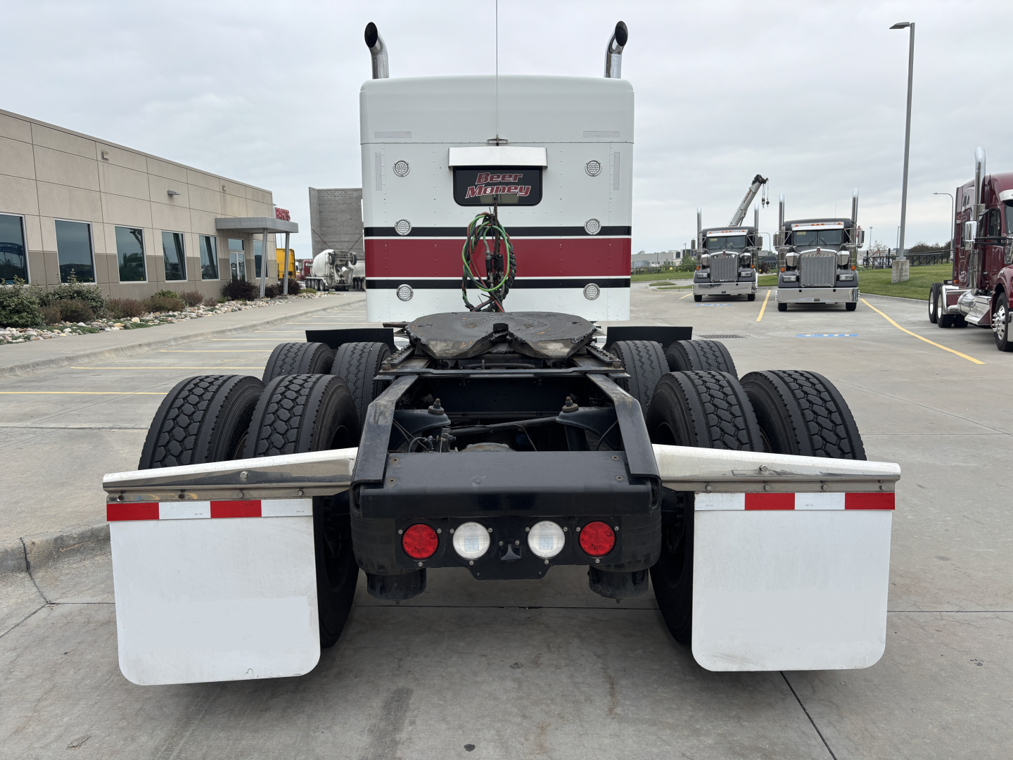 Kenworth W900L tractor rear view showing dual rear axles, fifth wheel, and mudflaps with rear lights and bumper.