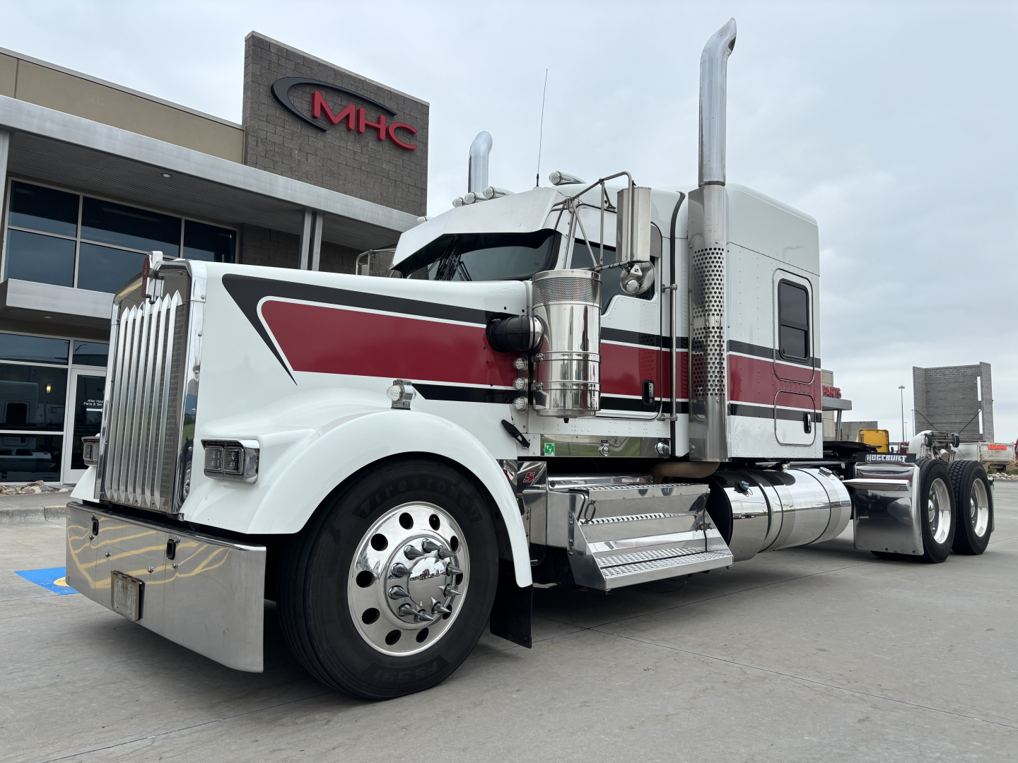 Kenworth W900L conventional sleeper truck side view showing chrome exhaust stacks and white red black livery.