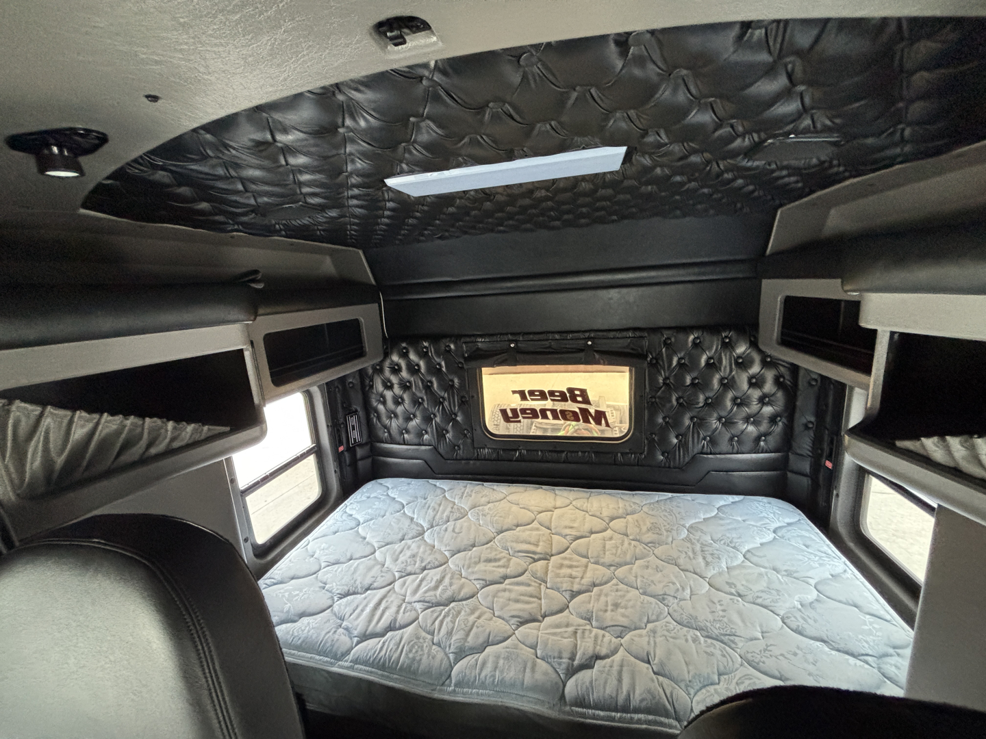 Kenworth W900L sleeper cab interior with quilted black ceiling and tufted headboard, diamond-stitched mattress, side cabinets, and a small plaque.