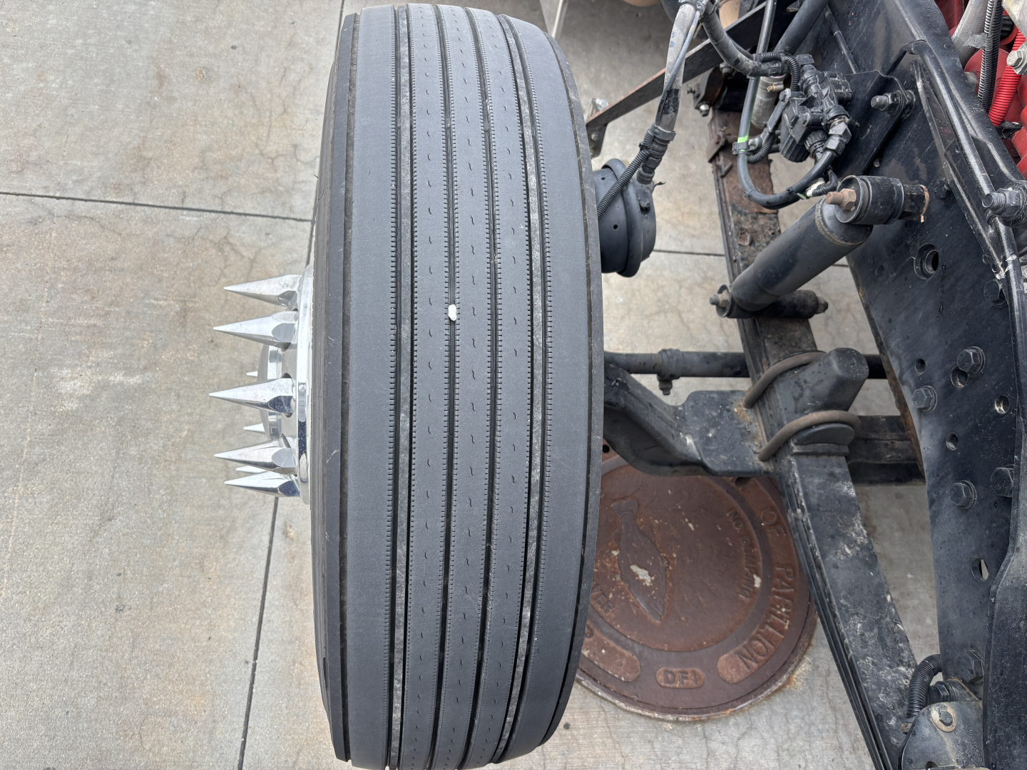 Kenworth W900L wheel with four-prong spike on tread area and chassis components visible.
