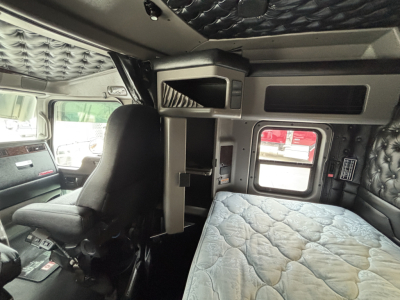 Kenworth W900L cab interior showing bunk area and control panel with quilted cab insulation and compact storage shelf.