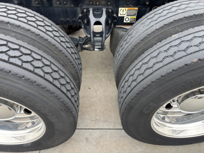 Dual rear tires of a Kenworth W900L tractor showing tread, chrome wheels, and a portion of the axle assembly between the two wheels.
