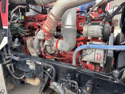 Kenworth W900L engine bay showing red engine blocks, large intake hoses, and various metal components.