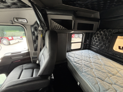 Cab interior of a Kenworth truck sleeper with bed mattress, overhead cabinets, and window; no legible small text visible