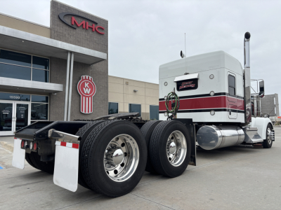 Kenworth W900L tractor truck in front of dealership with moderne cab and dual rear axles, chrome fuel tank and exhaust, visible Kenworth emblem on door