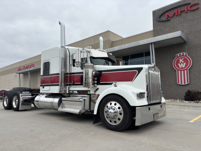 Kenworth W900L conventional sleeper truck in white with red stripe parked outside dealership showroom.