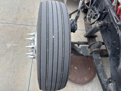 Kenworth W900L wheel with four-prong spike on tread area and chassis components visible.