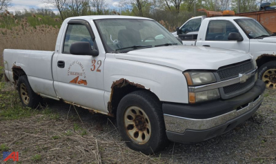 White 2005 Chevrolet Silverado 1500 pickup with rust on rear fenders, number 32 on door, text 'HIGHWAY 4' near front fender, black grille, two-tone bumper, other older trucks in background.