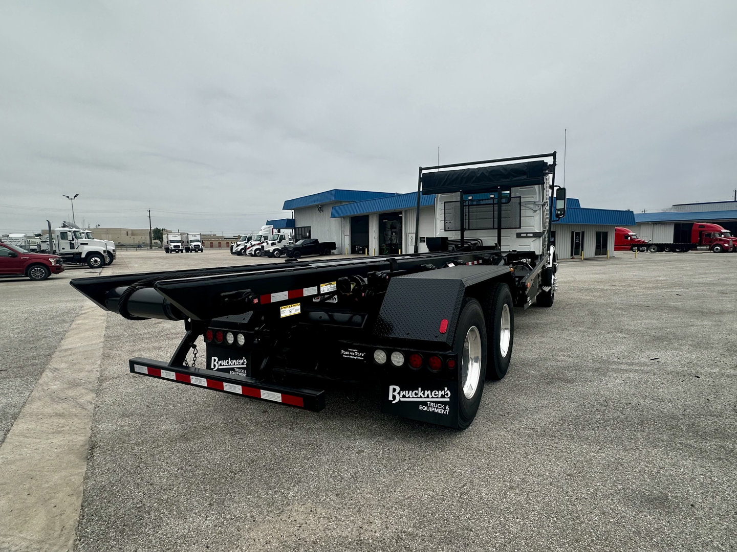 Rear view of a Volvo VHD64B300 roll-off truck on lot. Visible text includes Brackner’s (Brauckner's?) mudflaps, some small labels near rear but not legible.