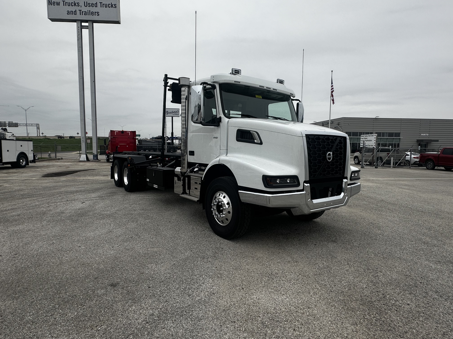 Volvo VHD64B300 rolloff truck in white, front three-quarter view, with chassis extending for container, dealership lot in background.