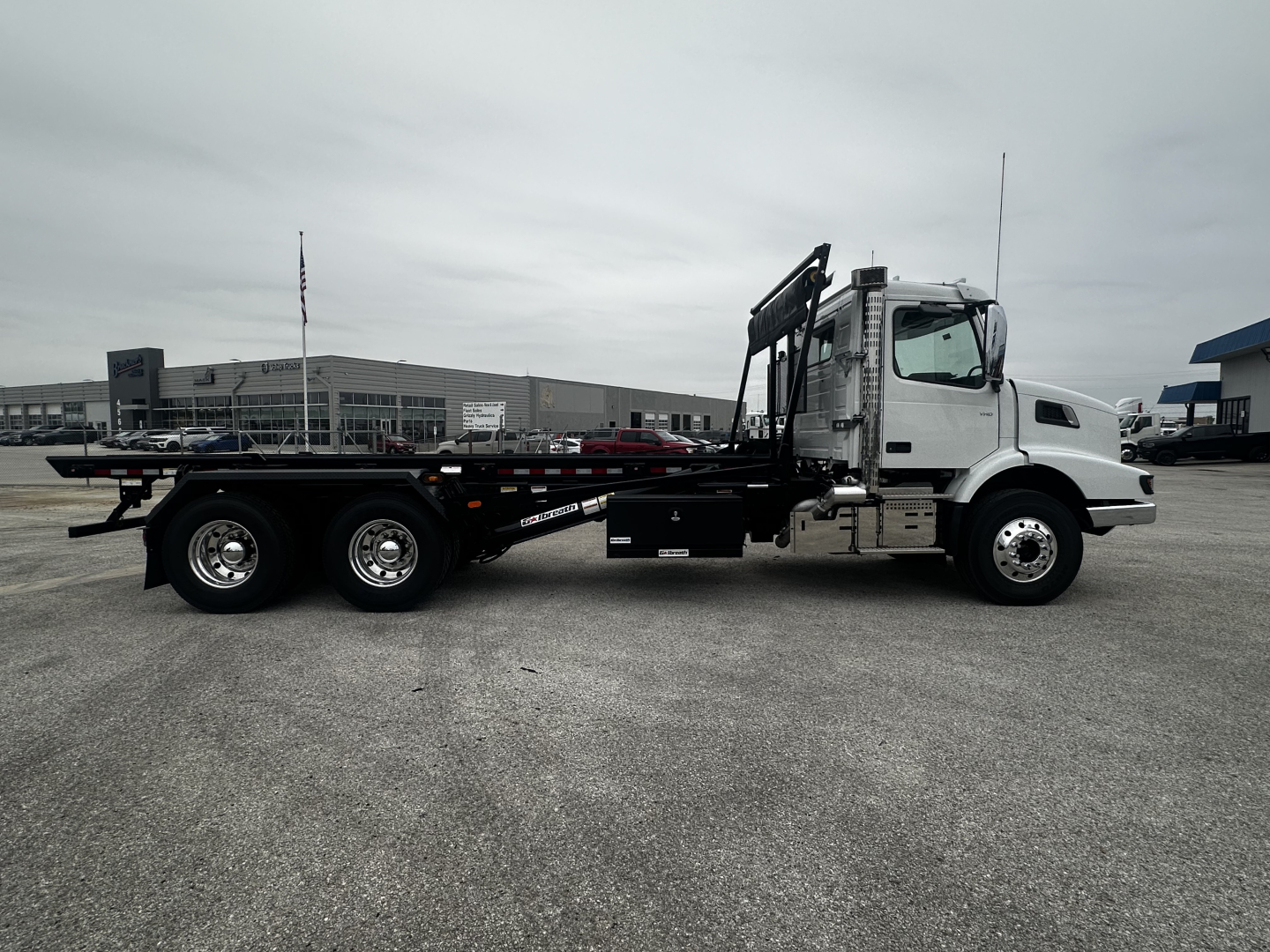 Volvo VHD64B300 rolloff truck side view showing long flatbed with hydraulic arms and cab, VIN 4V5KC9DHXTN710406.