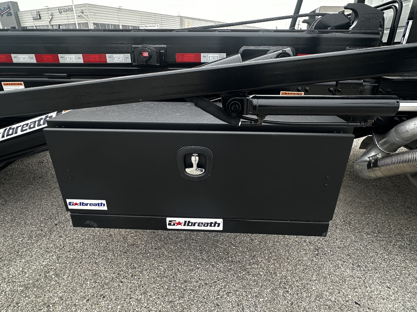 Volvo VHD64B300 rolloff truck side view showing a black Albreath toolbox mounted underframe with key lock and hydraulic lines.