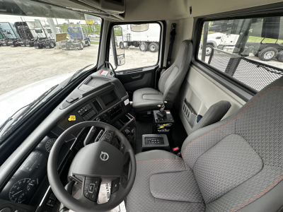 Cab interior of a Volvo VHD64B300 roll-off truck showing steering wheel, dashboard, driver seat, and passenger seat with gray fabric and orange stitching.