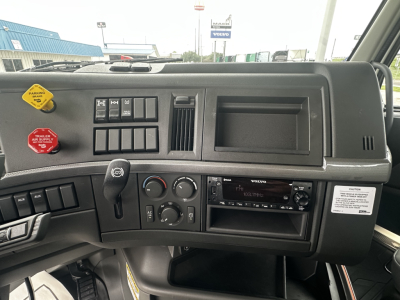 Dashboard of a Volvo truck cab showing switches, vents, and stereo head unit with controls and storage compartment.