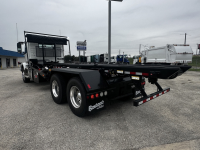 Flatbed tow truck 3-axle rear view showing aluminum flatbed and wheel fenders with tire racks and rear safety bumper.
