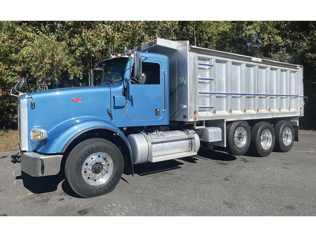 Peterbilt 367 dump truck side view showing blue cab and silver dumping bed with three rear axles.