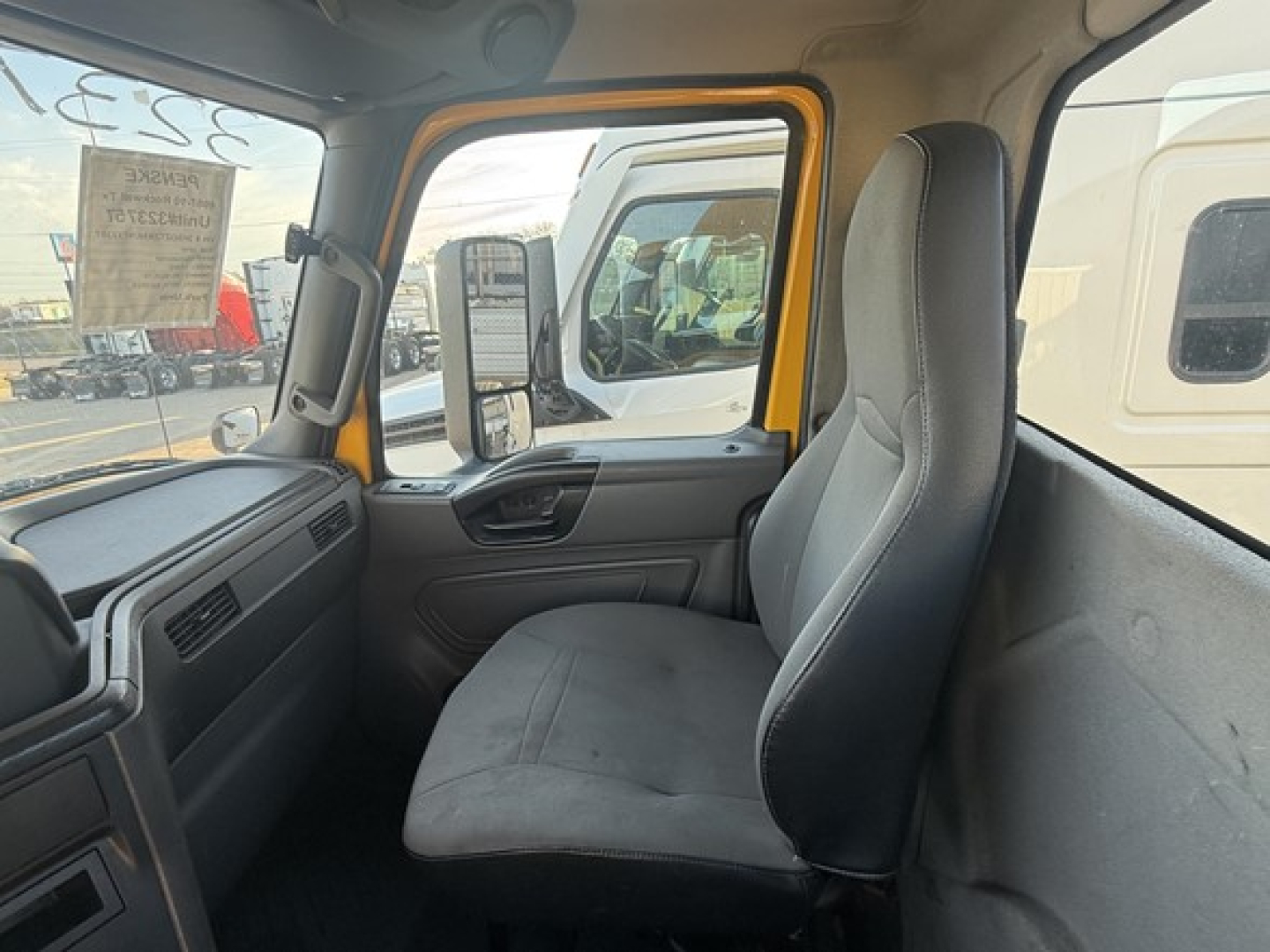 Cab interior of a 2019 International LT625 truck showing front bench seat, grey upholstery, yellow door frame, and side mirror view.