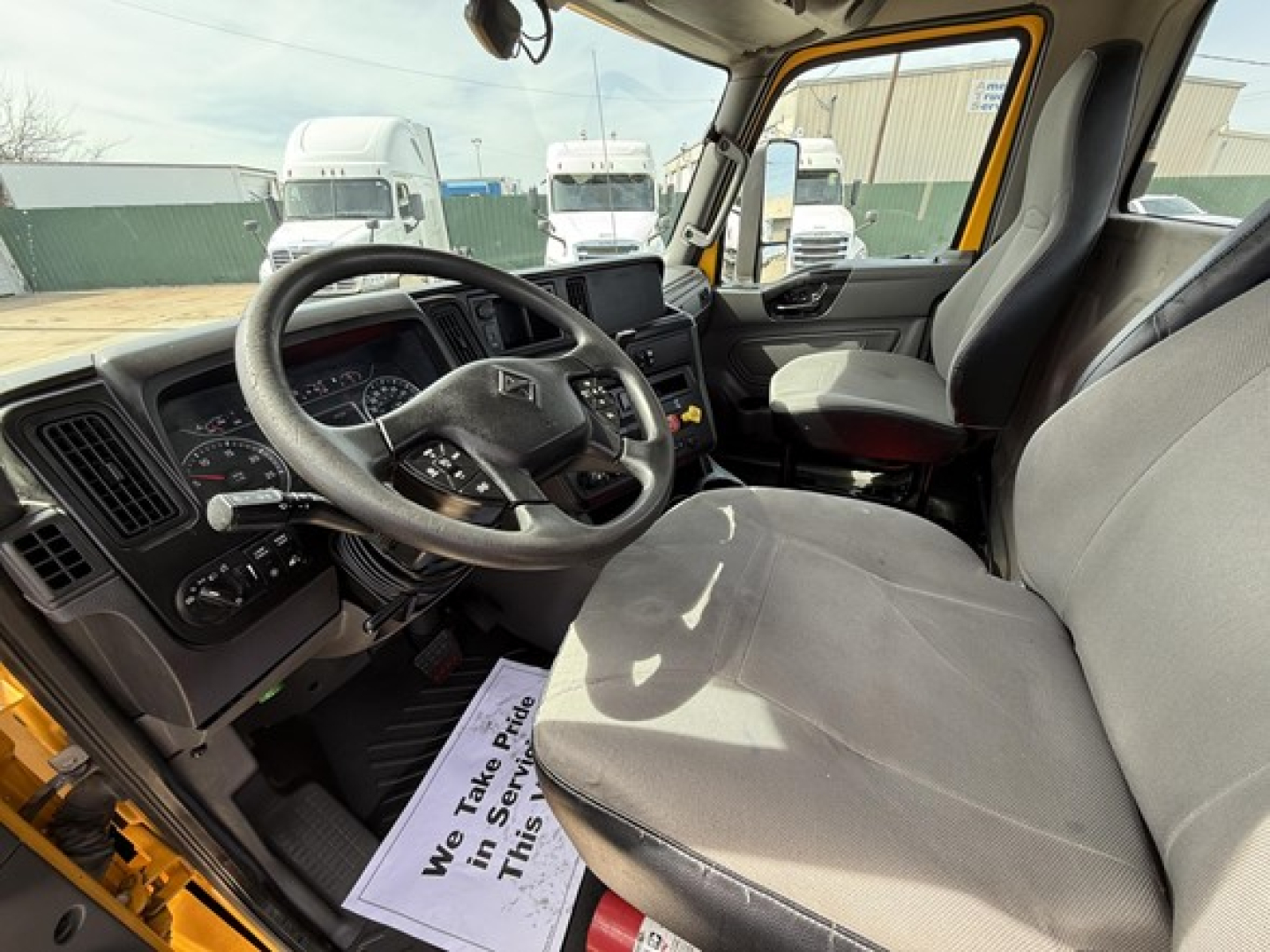 Interior cockpit of a 2019 International LT625 daycab showing steering wheel, dashboard, driver and passenger seats, and gear shifter with light from outside.