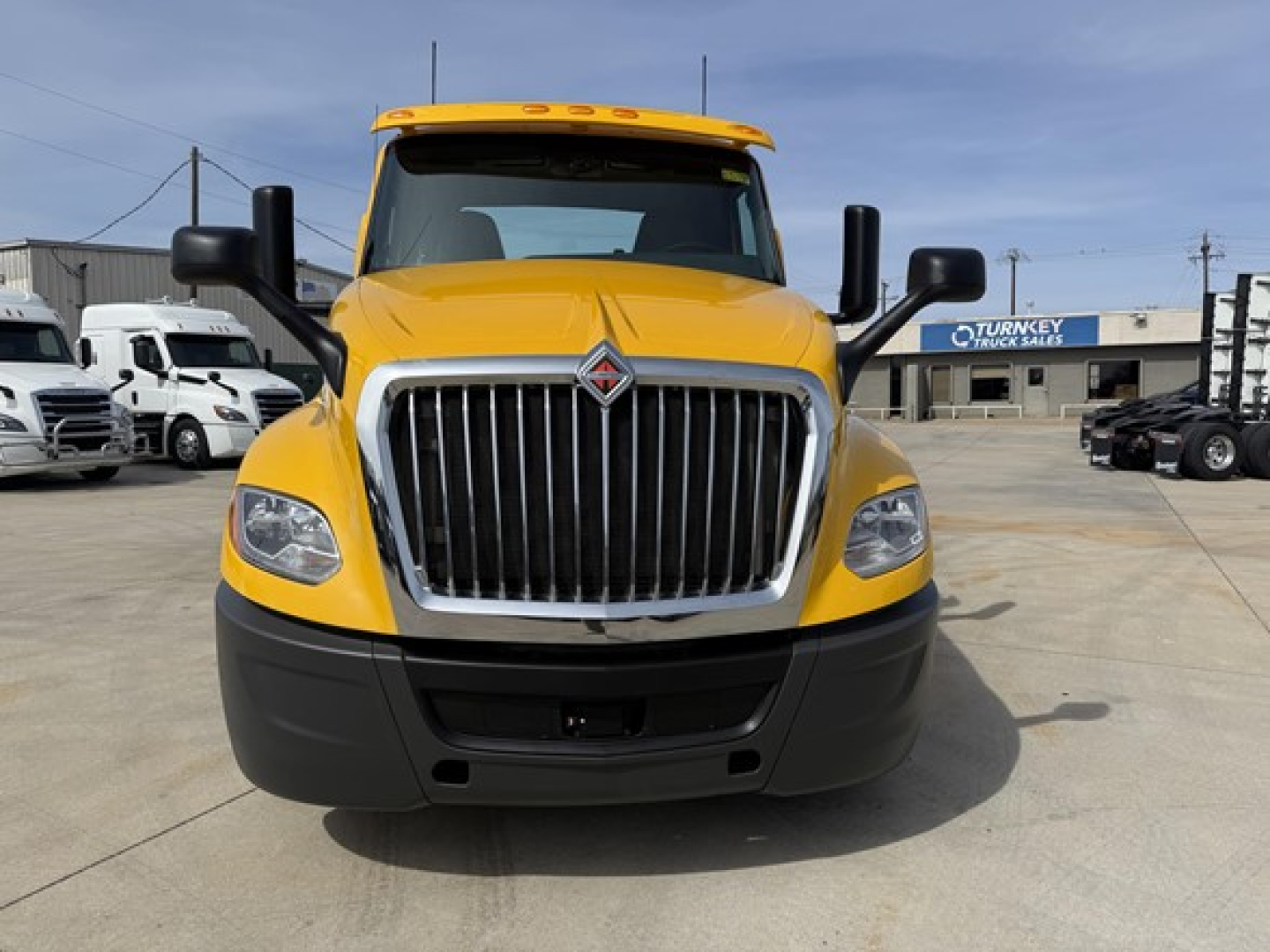 Truck front view showing bold chrome grille and yellow cab, International LT625 emblem not visible, large black bumper, headlights, and side mirrors.