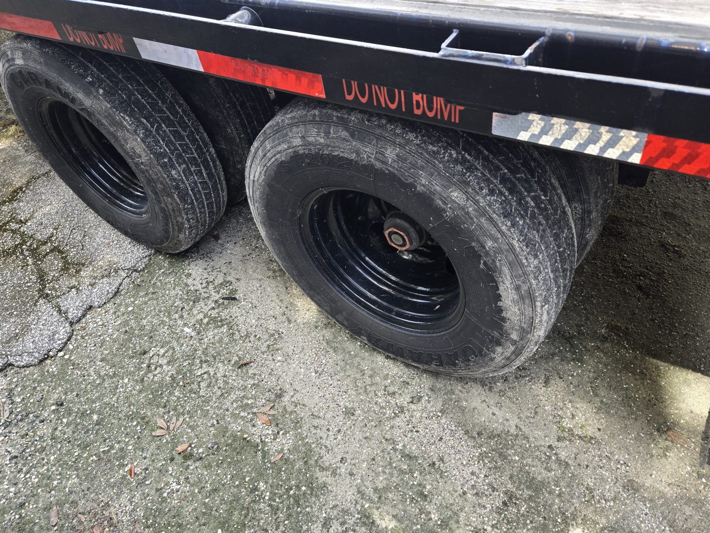 Trailer wheels and part of flatbed with black rims and muddy tires showing two axles, side rails, and reflective tape.