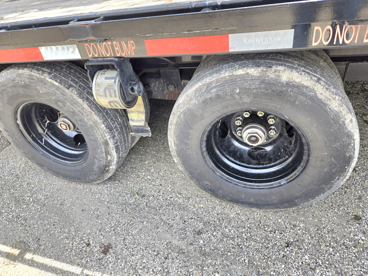 Trailer axle with dual tires and a wheel chock visible under the Gooseneck trailer.