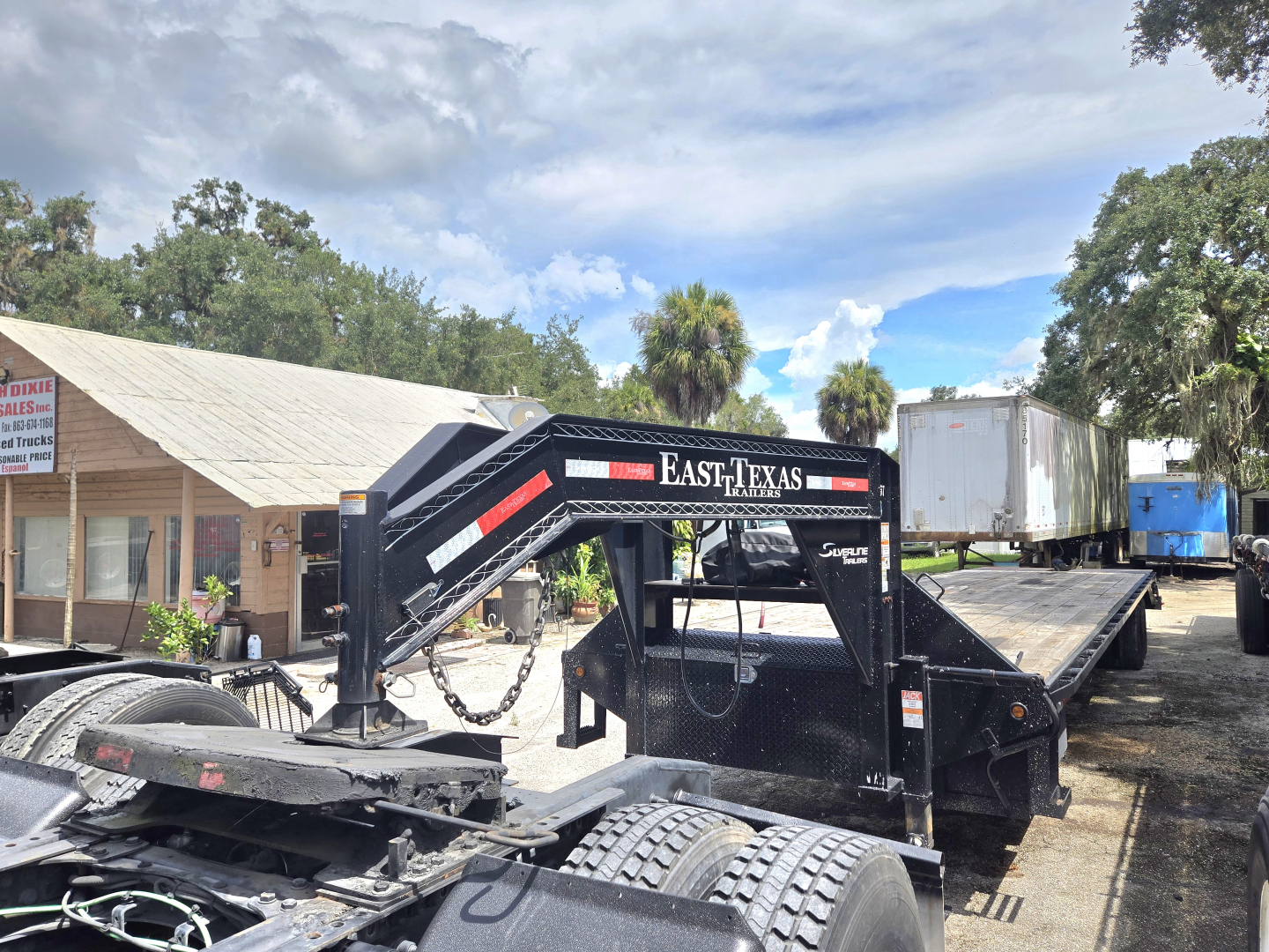 Low-angle view of a flatbed trailer with a gooseneck ramp system, labeled East Texas, in a used-trailer lot.