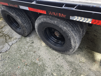 Trailer wheels and part of flatbed with black rims and muddy tires showing two axles, side rails, and reflective tape.