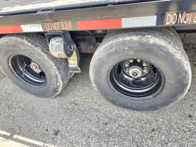 Trailer axle with dual tires and a wheel chock visible under the Gooseneck trailer.